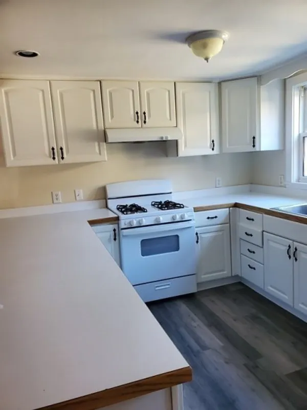 Bright kitchen with white cabinets, gas stove, and wood-look flooring near a window.
