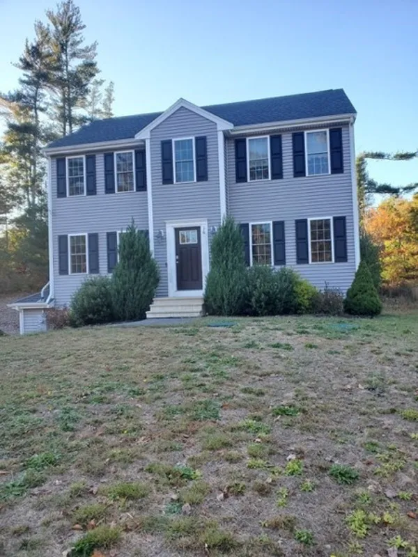 Two-story gray house with black shutters and shrubs in front, on a grassy lawn.