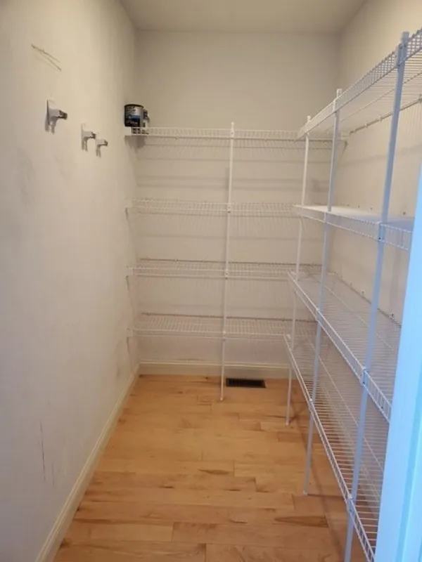 Empty pantry with white wire shelves and wooden floor, white walls, and hooks on the left.