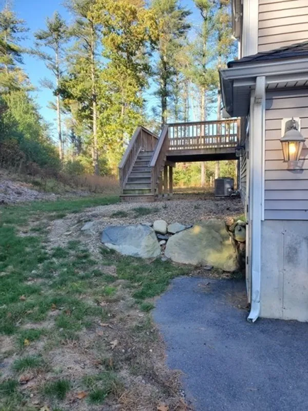 Backyard with a raised wooden deck, stairs, grass, rocks, and part of a house visible.