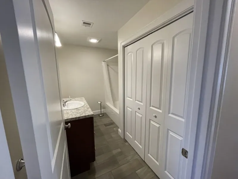 Bright bathroom with granite vanity, closed closet doors, and a bathtub with shower curtain.