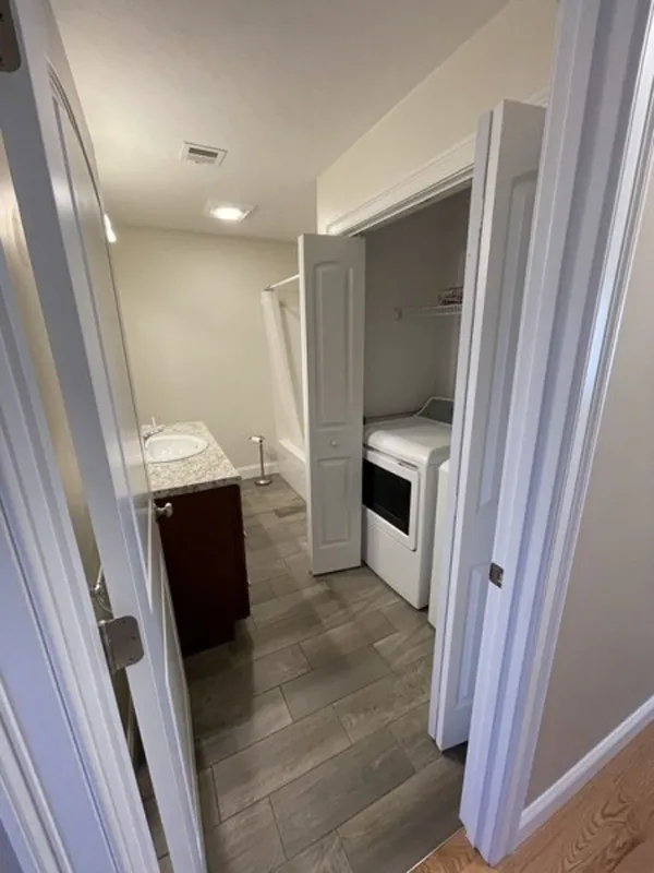 Bathroom with a washer and dryer in a closet, next to a vanity and bathtub.