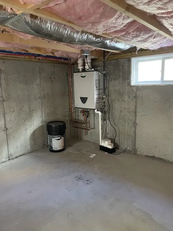 Unfinished basement with exposed insulation, a boiler unit, and a single small window.