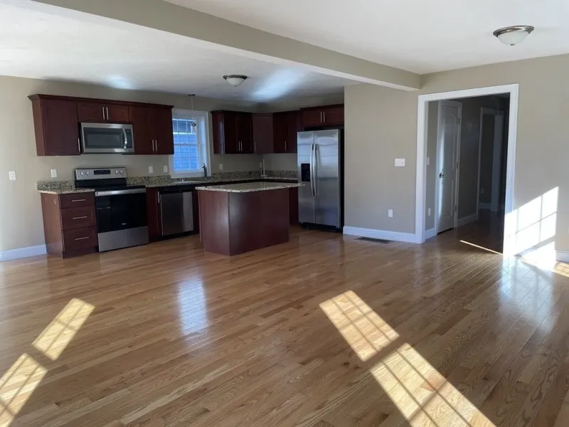 Empty kitchen with stainless steel appliances, wood cabinets, and hardwood floors.