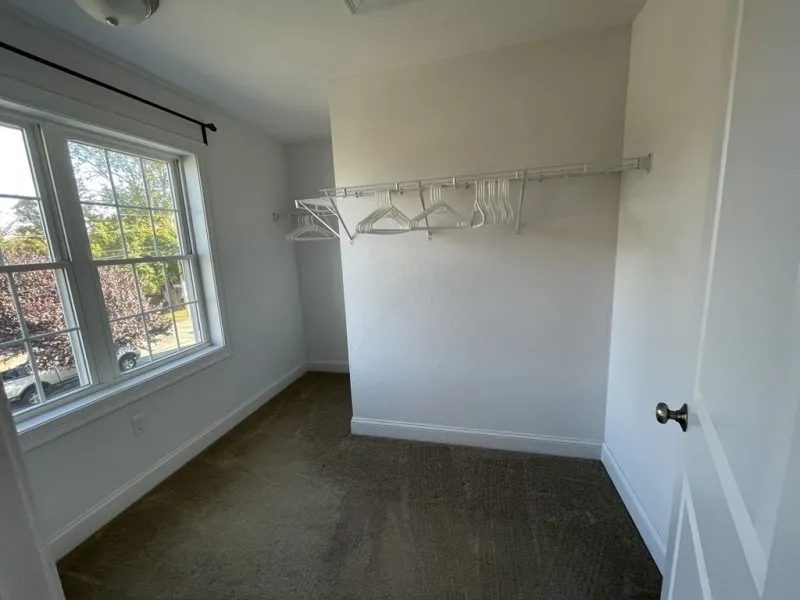 Empty walk-in closet with hangers on a rack and a window letting in natural light.