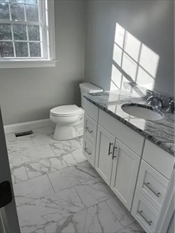 A bright bathroom with marble tile, a toilet, and a vanity with a marble countertop.