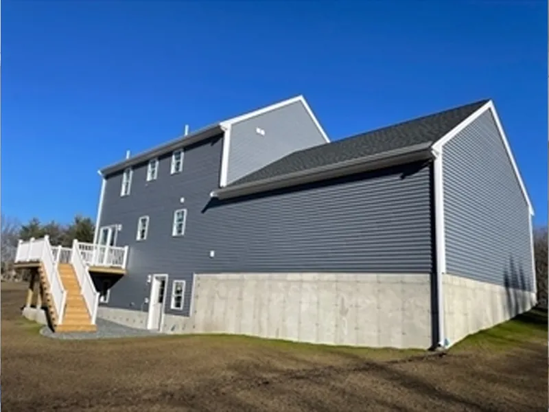 A large gray house with white trim, a deck, stairs, and a concrete foundation.