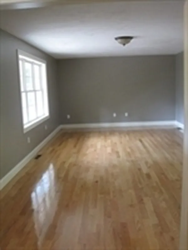 Empty room with light wood floors, gray walls, and a window on the left wall.
