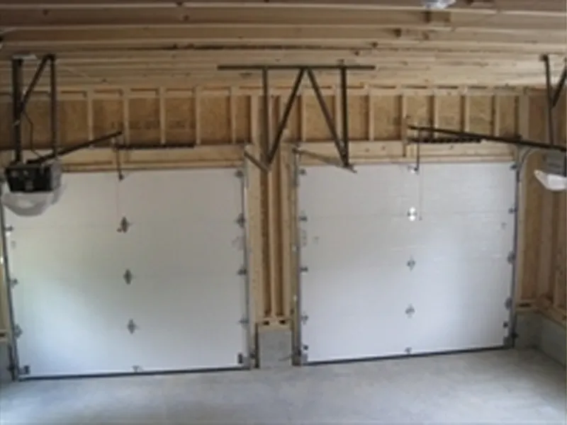 Two closed white garage doors in an unfinished garage with exposed wooden beams.