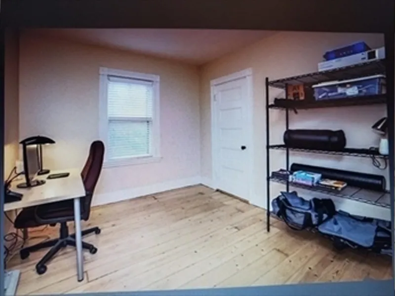 Small home office with a desk, chair, lamp, and metal shelving on a wooden floor.