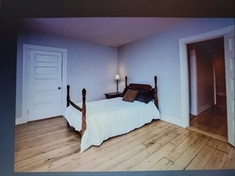 A simple bedroom with a wooden bed, white bedding, and wooden floorboards.
