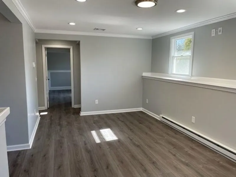 A bright, empty room with gray walls, wood floors, and a window letting in sunlight.