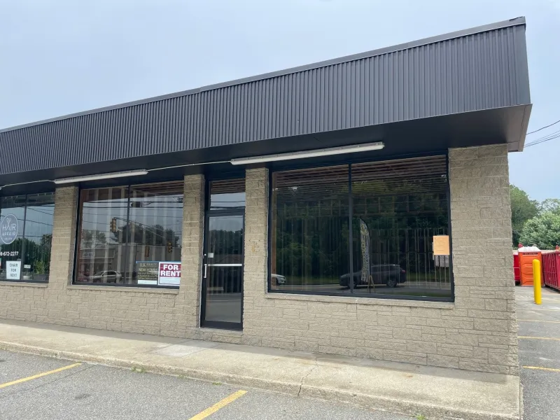 A vacant storefront with large windows and a For Rent sign in one window.
