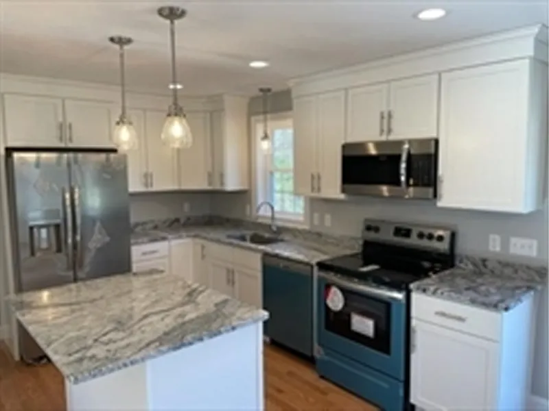 Modern kitchen with white cabinets, marble countertops, and stainless steel appliances.