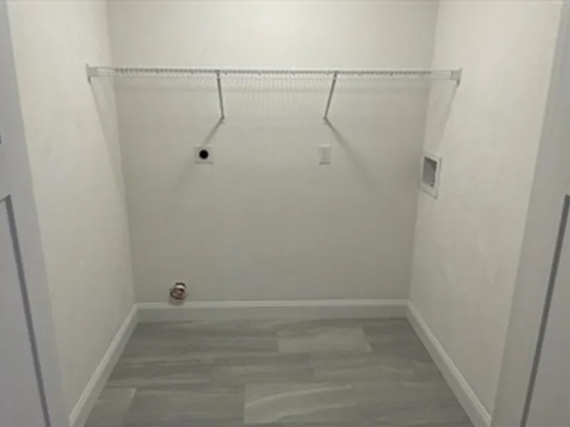 Empty laundry room with wire shelf, hookups for washer and dryer, and gray tile floor.