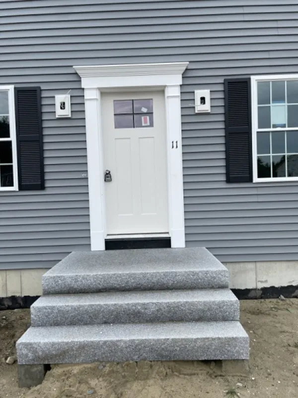 Gray house with white front door, three granite steps, and black shuttered windows.
