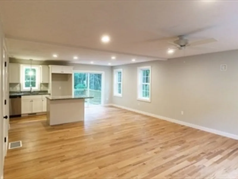 Open-plan kitchen and living room with wood floors, white walls, and large windows.