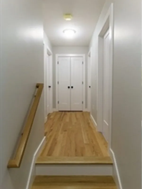 A hallway with wooden floors, white walls, and four white doors at the end.