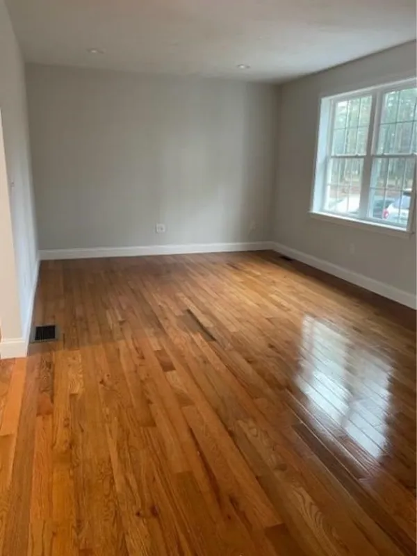 Empty room with polished wood floors, white walls, and large windows letting in natural light.
