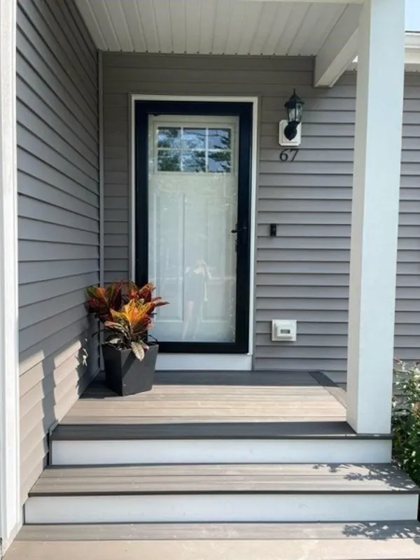 Front porch with gray steps, a black door, potted plant, and house number 67.
