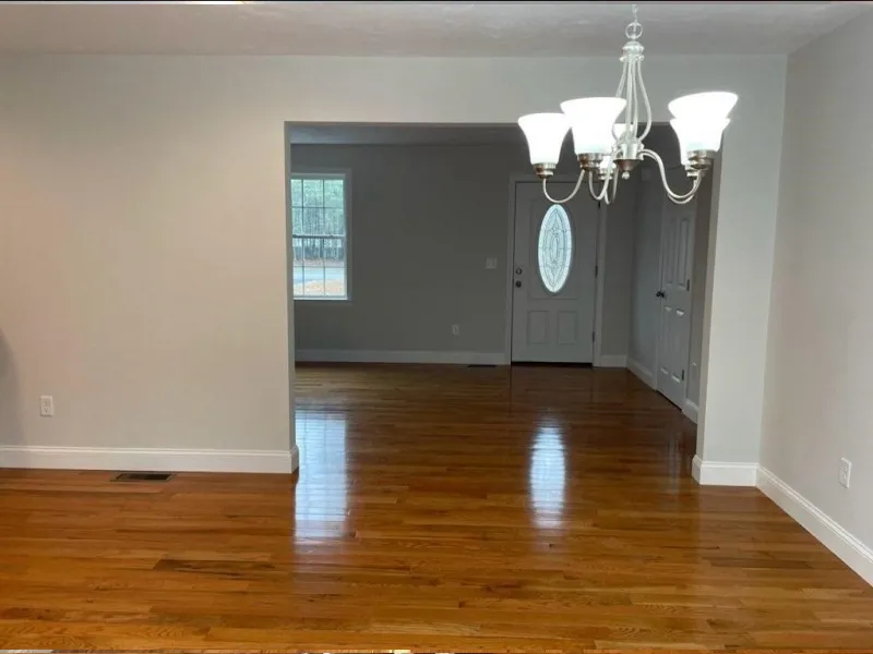 Bright room with hardwood floors, a chandelier, and a view of a door and window.