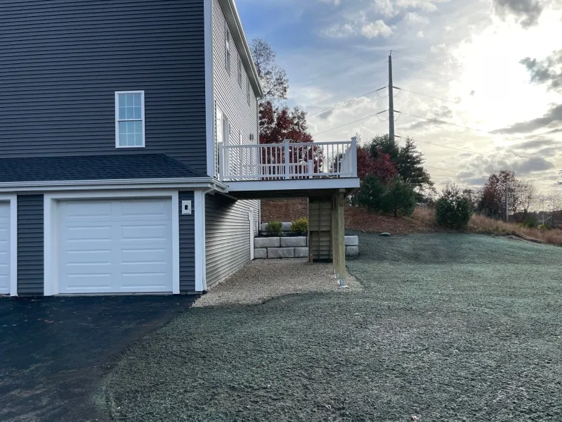A gray house with a small raised deck and a double garage, next to a grassy yard.