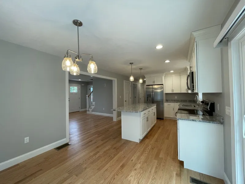 Modern kitchen with white cabinets, island, pendant lights, and wood flooring.