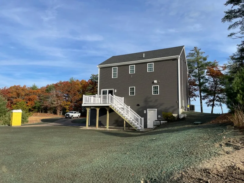 Two-story gray house with white stairs, surrounded by trees and a gravel driveway.