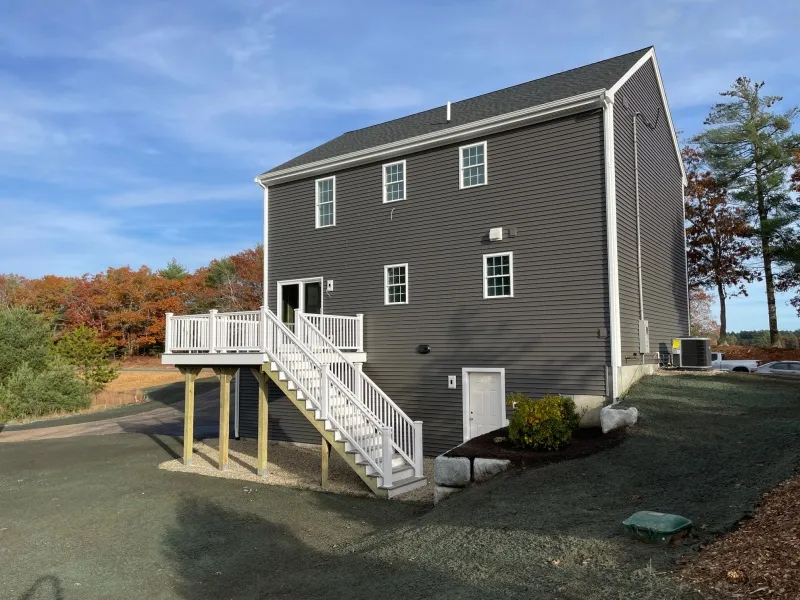 Gray two-story house with a raised white deck and stairs, surrounded by trees and grass.