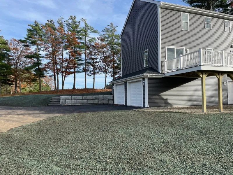 Gray two-story house with two garages, new grass, and trees in the background.
