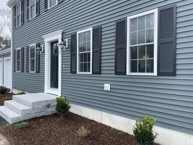 Gray house with black shutters, white trim, and small bushes planted by the front steps.