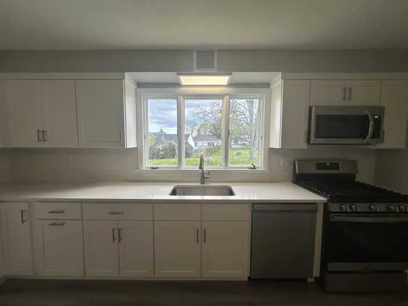 Modern kitchen with white cabinets, a large window, stainless appliances, and a gas stove.
