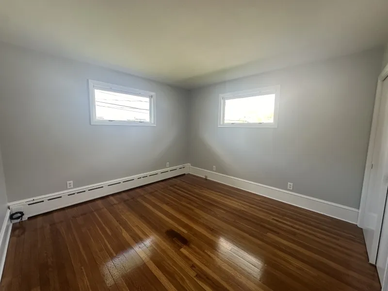Empty room with two windows, light gray walls, and shiny hardwood floor.