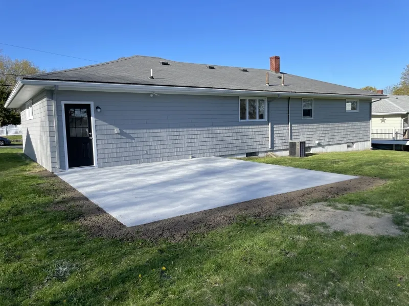 A concrete patio sits behind a gray house with a door and several windows.