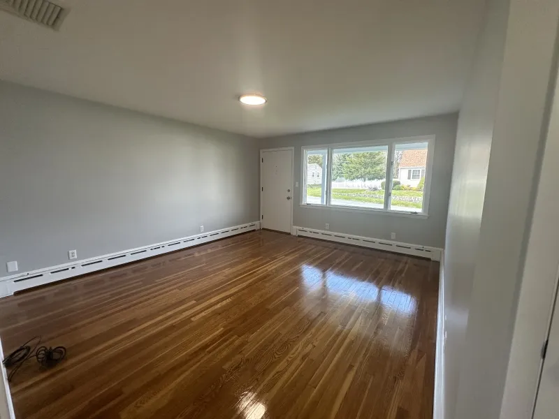 Empty room with polished wood floor, gray walls, large window, and ceiling light.