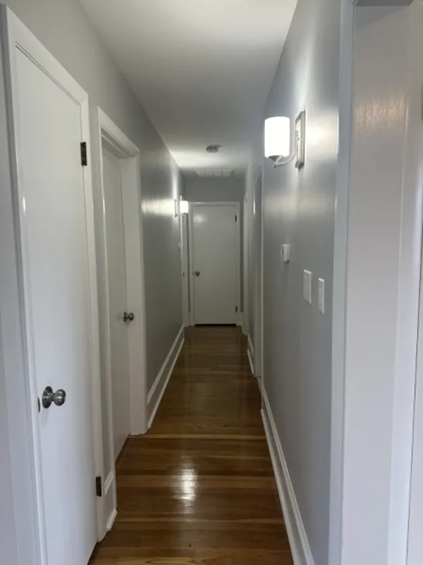 A bright hallway with wooden floors, gray walls, and several white doors on each side.