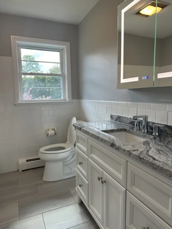 Modern bathroom with gray walls, marble countertop, and large mirror above the sink.
