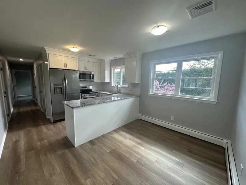 Modern kitchen with stainless steel appliances, wood floors, and large window with daylight.