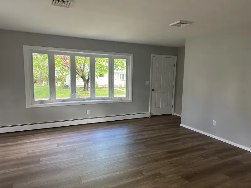 Empty room with gray walls, wood floors, large windows, and a white door.