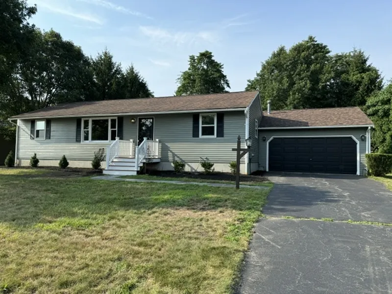 Single-story house with a front porch, attached garage, and driveway on a sunny day.