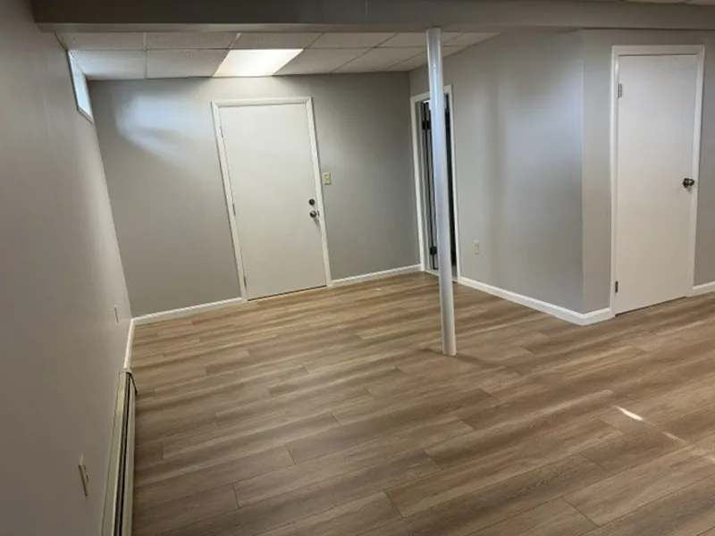 Room with light wood flooring, gray walls, white doors, and a ceiling support pole.
