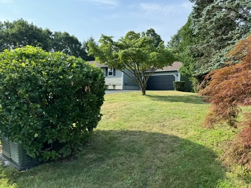 A gray house with a dark garage, surrounded by trees and a grassy lawn on a sunny day.