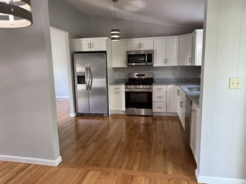 Modern kitchen with stainless steel appliances, white cabinets, and hardwood floors.
