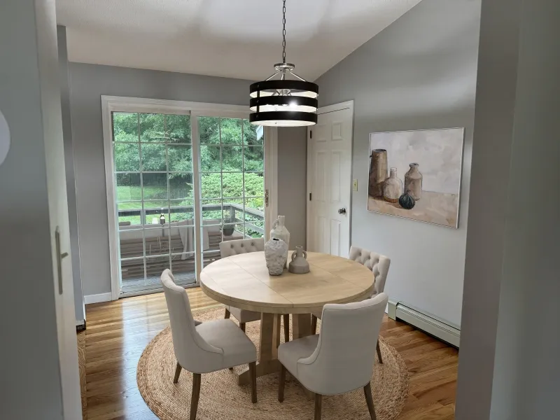 Bright dining area with round table, four chairs, and large window overlooking greenery.