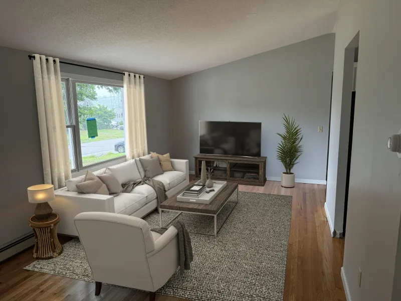 Bright living room with a sofa, TV, armchair, coffee table, and large window.