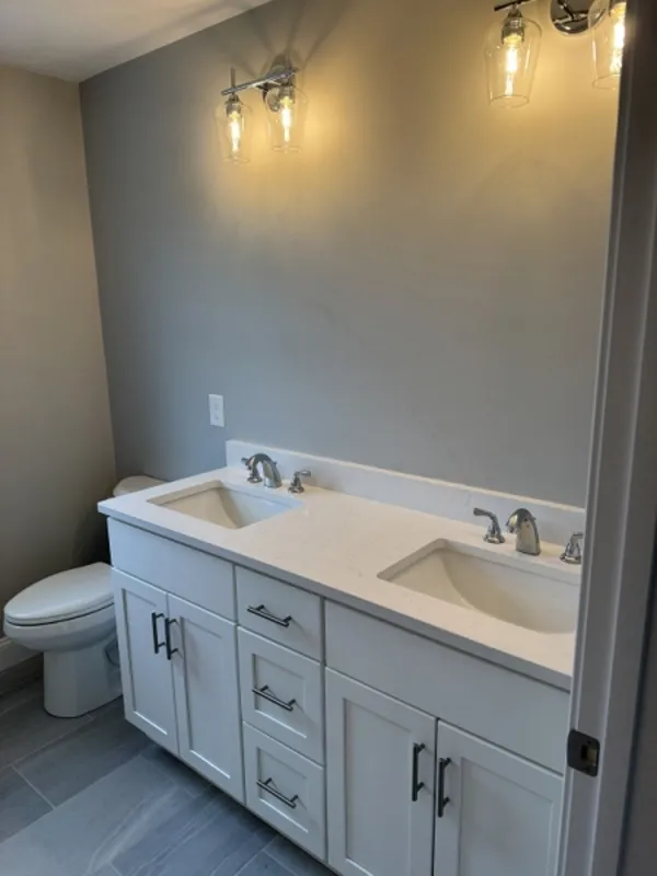 Modern bathroom with double sinks, white vanity, and wall-mounted lights above mirrors.
