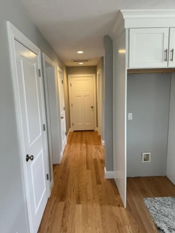 A hallway with wooden floors, gray walls, and white doors, lit by ceiling lights.