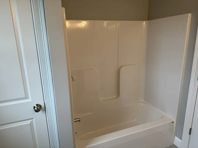 White bathtub and shower unit with a built-in seat in a bathroom with light-colored walls.