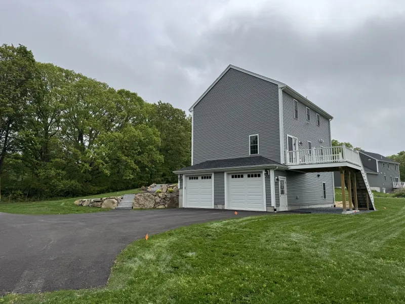 Gray two-story house with a three-car garage and driveway, surrounded by grass and trees.