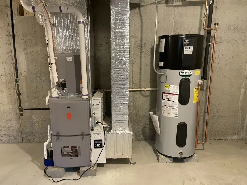 Furnace and water heater installed in a basement with unfinished concrete walls.